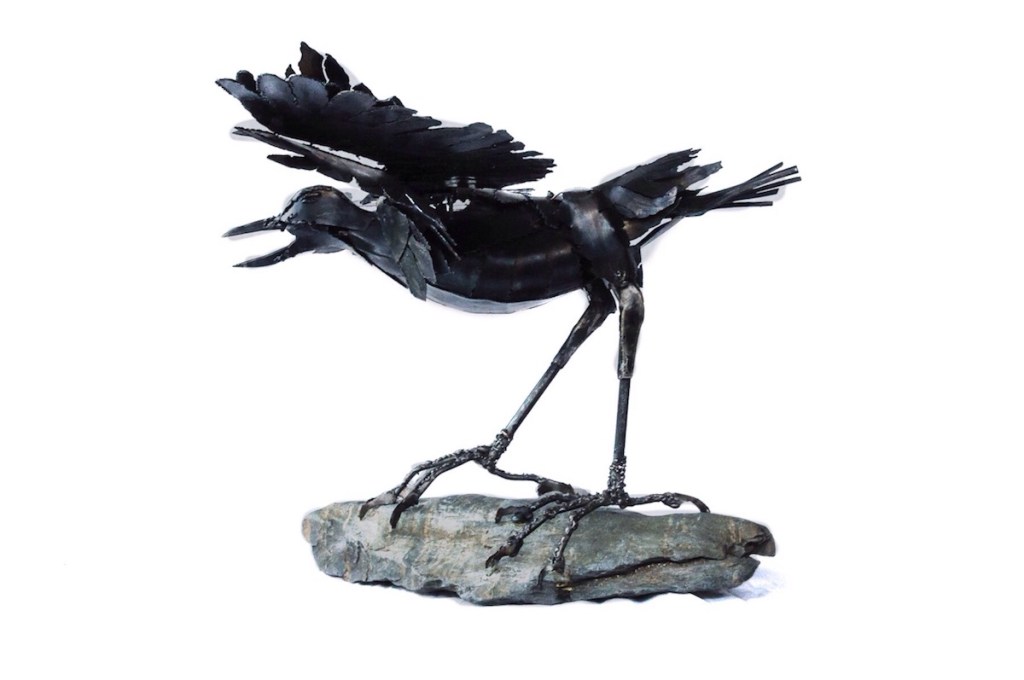 Side view. Sculpture of Arnold an aggressive crow on stone base. Arnold is protecting and though a crow has the heart of an eagle. Made from mild steel.  